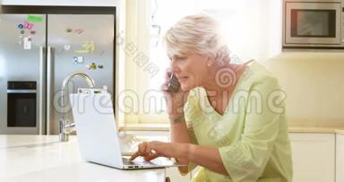 在厨房使<strong>用笔记本电脑</strong>的时候，一位年长的<strong>女士</strong>在说手机